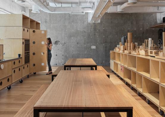 a woman standing in a room with wooden tables