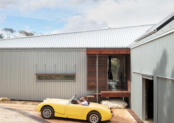 a man driving a yellow convertible car in front of a house