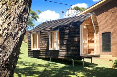 a small wooden house with a tree in the back